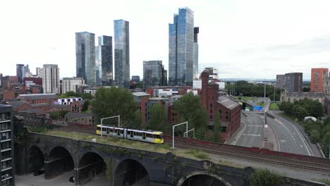 Aerial-drone-flight-alongside-a-tram-on-a-bridge-showing-a-background-of-Manchester-City-Centre-skyscrapers-and-apartment-buildings
