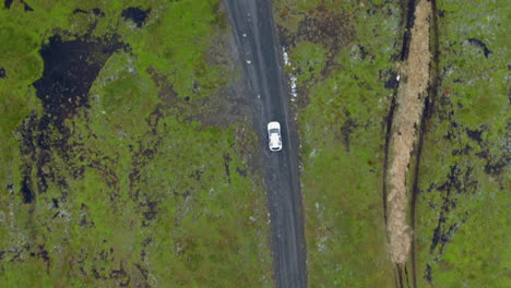 Aerial-top-down-of-white-car-on-muddy-dirt-road-with-potholes
