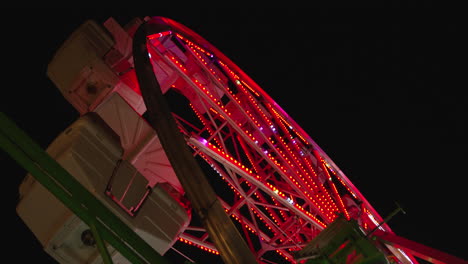 A-low-angle-shot-of-a-Ferris-wheel-tilts-up-to-reveal-the-top-of-it-as-gondolas-swing-in-the-wind-at-night-and-the-lights-of-the-Ferris-wheel-change-colors