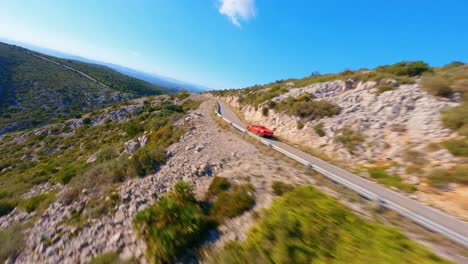 Aerial-view-of-a-Red-Ferrari-driving-along-a-scenic-mountain-highway-in-Spain