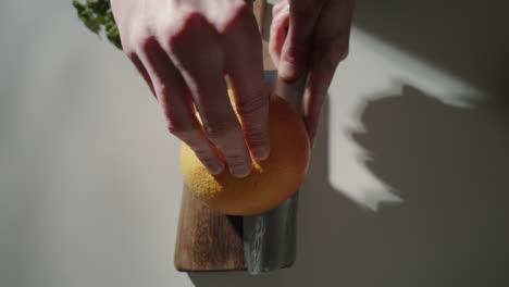 Hands-cutting-grapefruit-in-half-in-the-kitchen-at-home-on-wooden-cutting-board-with-sharp-knife