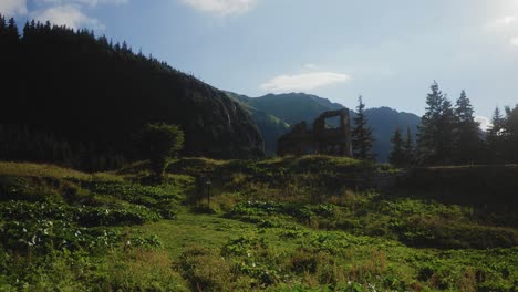 Slow-right-panning-shot-of-a-mountain-meadow-with-a-cabin-in-ruins-in-the-summer-sun
