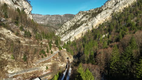 Coches-Circulando-Por-La-Carretera-En-Las-Gargantas-Del-Jura-En-Moutier-En-Suiza-En-Un-Frío-Y-Soleado-Día-De-Otoño-Con-Nieve-En-Las-Montañas-Al-Fondo