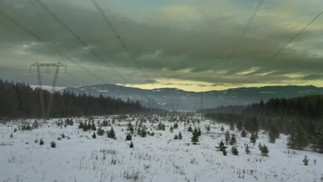 Electricity-in-Motion:-Close-Up-Drone-Shot-of-Powerlines-in-a-Snowy-Mountain-Landscape-at-Sunse