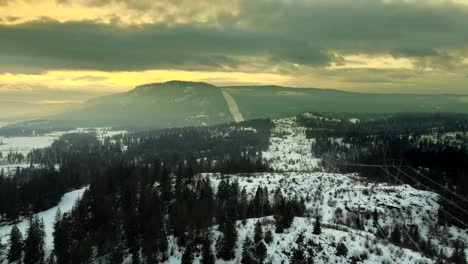 Spektakuläre-Luftaufnahme-Von-Stromleitungen,-Die-Bei-Sonnenuntergang-über-Einem-Verschneiten-Wald-Aufragen