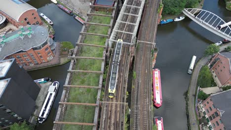 Aerial-drone-flight-over-Castlefield-Quays-with-a-birdseye-view-following-a-tram-on-a-bridge-and-slowly-tilting-up-to-reveal-a-view-of-Manchester-City-Centre-skyscrapers