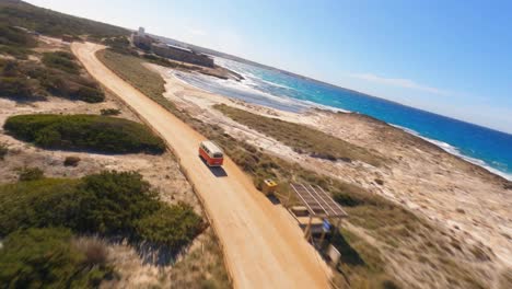 FPV-aerial-following-a-VW-minibus-driving-along-a-picturesque-oceanside-highway