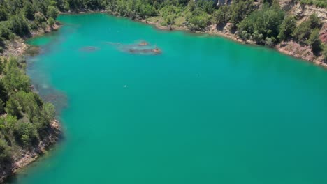 Aerial-drone-Flying-Over-Vibrant-Turquoise-Lake-Surrounded-By-Trees-With-Birds-Flying-Over-It