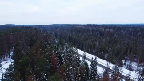 Aerial-reveal-of-empty-highway-through-snow-covered-forest-on-overcast-day