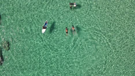 Aerial-top-down-view-of-people-in-surfboards-and-sea-scooters-enjoying-the-clear-water-at-Cala-Escondida-in-Ibiza,-Spain