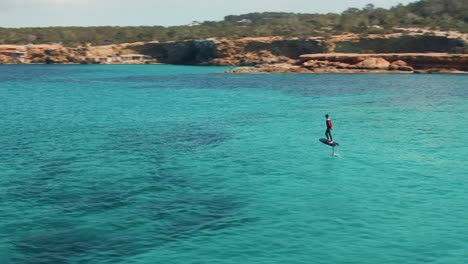 Aerial-view-of-a-surfer-surfing-in-the-blue-water-of-Cala-Escondida,-Spain