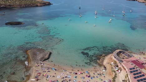 Drohnenaufnahmen-über-Dem-Strand-Von-Cala-Escondida-Auf-Der-Insel-Ibiza-Und-Dem-Yachthafen,-Wo-Viele-Boote-Vor-Anker-Liegen