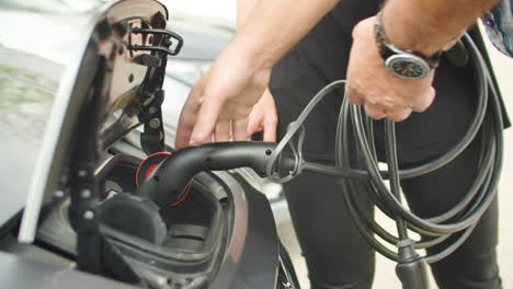 The-hands-of-a-man-connecting-one-end-of-a-cable-to-the-battery-of-an-electric-car