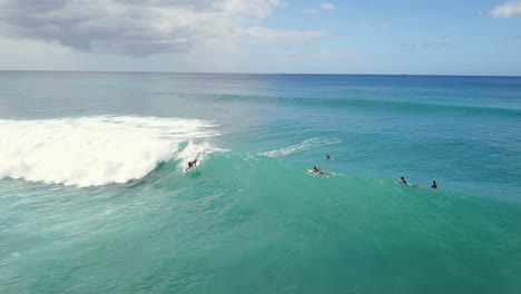 Surfer-paddles-onto-large-wave-spraying-and-carving-reverse-aerial-tracking