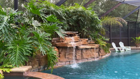 Wide-view-of-outdoor-swimming-pool-with-waterfall-and-bamboo-inside-screened-in-lanai-porch