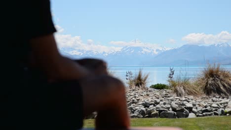 Young-man-sitting-on-outside-bench-drinking-coffee-while-taking-in-breathtaking-view-of-Mount-Cook,-New-Zealand