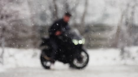 Out-of-focus-slow-motion-of-a-young-man-starting-a-black-motorcycle,-with-snow-falling-down