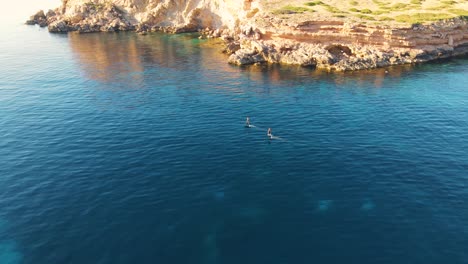 Aerial-View-Of-Two-People-Surfing-Across-Waters-Off-Cala-Escondida-Coastline-On-Electric-Wakeboards