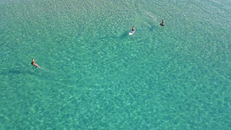 Vista-Aérea-De-Gente-Surfeando-Con-Tableros-Eléctricos-Efoil-En-Las-Aguas-Claras-De-Cala-Escondida-En-Ibiza,-España