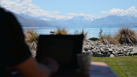 Person-typing-on-computer-outside-with-stunning-views-of-Mount-Cook-and-Lake-Pukaki