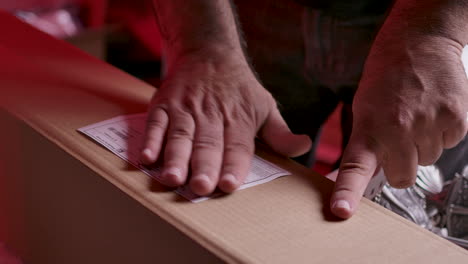 The-hands-of-a-male-warehouse-worker-putting-an-adhesive-label-with-the-printed-shipping-information-on-a-boxed-item