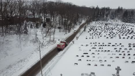 Snowplow-in-a-road-next-to-a-cemetery-covered-with-snow