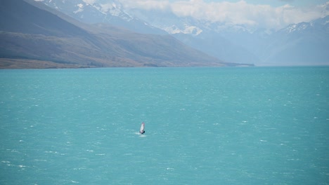Windsurfer-on-striking-aquamarine-lake,-snowy-mountain-background