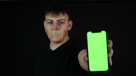 Cyber-Bullying-Concept,-Young-Man-With-Tape-Over-Mouth-Holding-Smartphone-With-Green-Screen