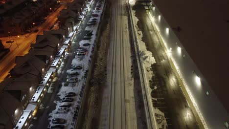 Snow-covered-railway-tracks-near-private-estates,-aerial-drone-night-view