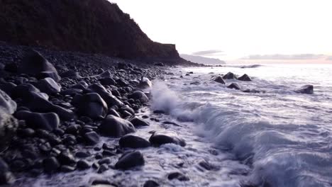 Drone-flying-low-over-Volcanic-beach,-Waves-rolling-onto-black-beach-pebbles,-Madeira-Island