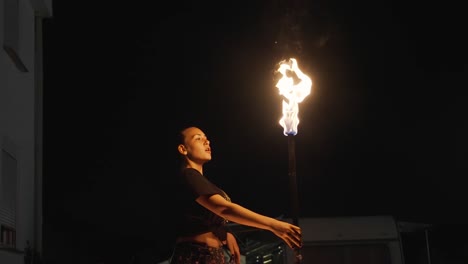 Female-Fire-Eater-at-Night,-Holding-Torch-and-Blowing-Fuel-on-Flame,-Slow-Motion
