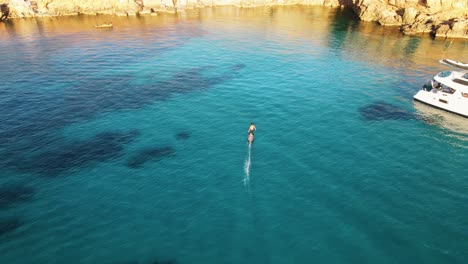 Aerial-View-Of-Male-Using-Electric-Surfboard-Across-Turquoise-Waters-Off-Cala-Escondida-Coastline