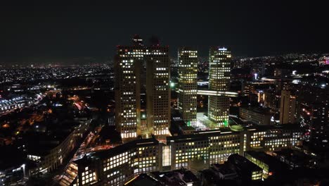 Aerial-view-away-from-the-Arcos-Bosques-complex,-nighttime-in-Mexico-city---pull-back,-drone-shot