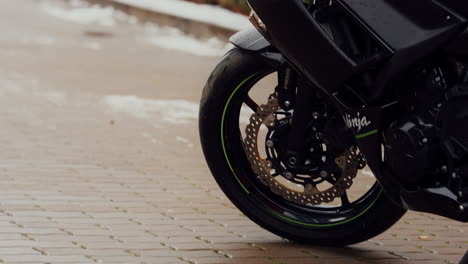 New-tire-detail-of-a-parked-black-motorbike,-on-a-snowy-day