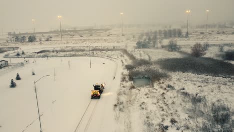Mini-bulldozer-drives-through-empty-parking-lot,-snow-covered,-storm