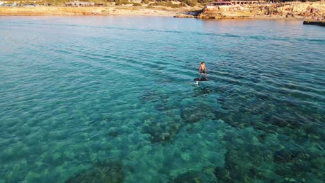 Drone-footage-follows-a-person-surfing-on-a-fliteboard-over-the-crystal-clear-and-azure-waters-of-an-ocean-near-the-shoreline