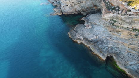 Luftaufnahme-Des-Blauen-Wassers-Und-Der-Felsen-Von-Cala-Escondida,-Spanien