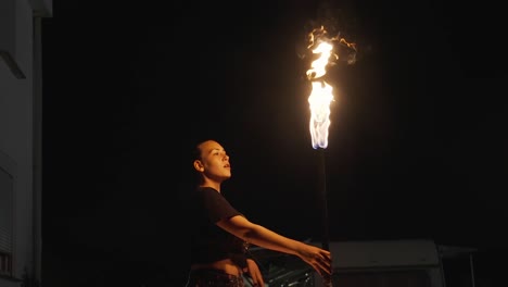 Beautiful-female-fire-eater-looks-at-camera-then-spits-alcohol,-kerosene-against-fire-torch-and-causes-big-flame