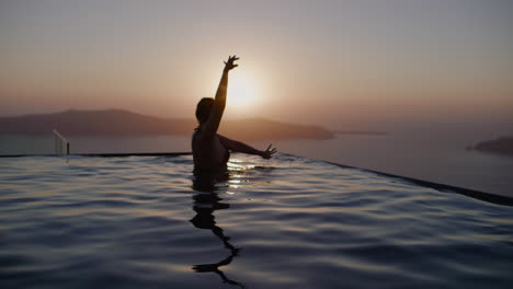 A-woman-dancing-in-infinity-pool-during-sunset-over-sea---Slow-motion,-Santorini,-Greece