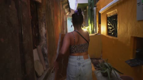 young-girl-carrying-a-painting-through-a-bright-colourful-alley-street,-with-the-sun-flaring