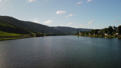 Flight-over-lake-Mosel-towards-a-bridge-next-to-a-villlage-and-vineyard