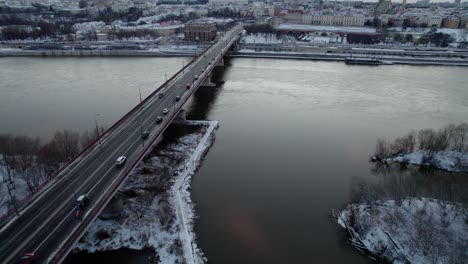Aerial-tracking-shot-of-vehicle-crossing-Vistula-River-during-snowy-day-in-Warsaw-City,Poland---Tilt-up