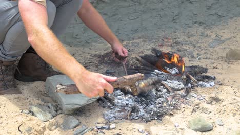 A-close-up-of-a-man-cooking-a-fish-bush-style-on-hot-coals-on-a-fire-on-the-coastline
