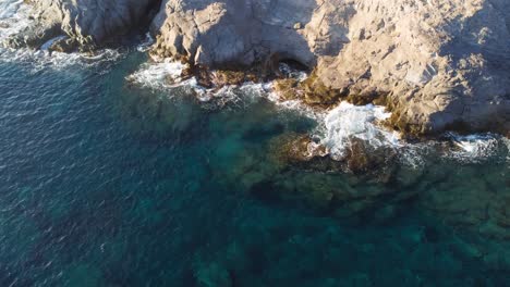 Stunning-topdown-aerial-view-of-blue-waves-crashing-on-rocks,-slow-lowering,-day