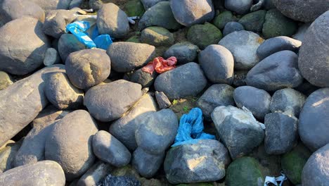 Rocky-river-bank-covered-in-trash,-a-stark-reminder-of-an-environmental-issue