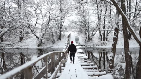Man-is-walking-over-a-bridge-covered-in-snow-in-a-winter-landscape,-cold-and-refreshing-weather-atmosphere