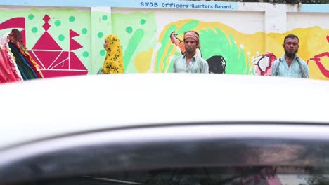 Bangladeschische-Rikschafahrer-Stehen-Auf-Dem-Bürgersteig-Einer-Belebten-Und-Farbenfrohen-Straße,-Während-Fahrzeuge-In-Dhaka,-Bangladesch,-An-Ihnen-Vorbeifahren