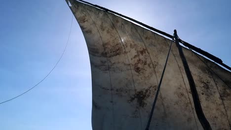 Old-dirty-sail-moving-back-and-forth-in-the-wind-against-the-blue-sky-blocking-the-sun