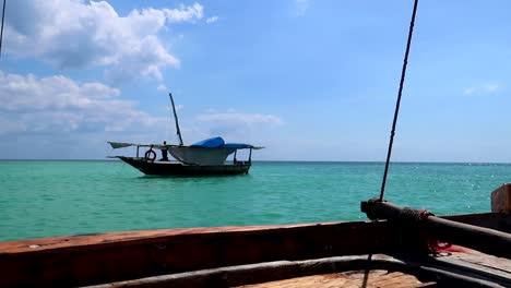Traditional-african-wooden-boat-with-a-sailor-seen-from-another-boat-navigating-in-the-turquoise-waters-of-Zanzibar,-Tanzania