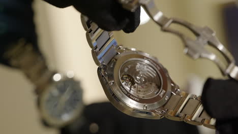 VERTICAL-Salesperson-inspecting-mechanical-clockwork-Piaget-wristwatch-back-reflecting-in-retail-store-display